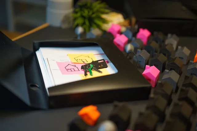 Keys and real estate documents on a desk surrounded by colorful house models, symbolizing property transactions. Sådan opstiller du en vægtet kriteriemodel til bureauvalg